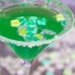 Close-up view of bright green Lucky Charms martini with green marshmallows and cereal rim on glass