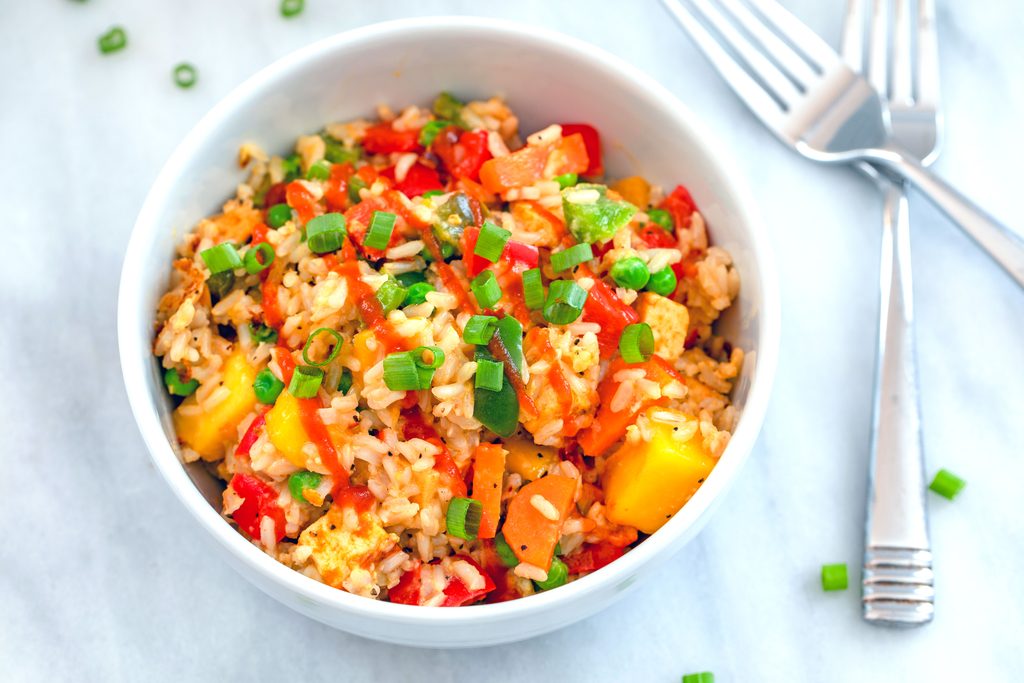 Landscape overhead closeup view of a bowl of mango coconut fried rice on marble surface with two forks and chopped scallions in the background 