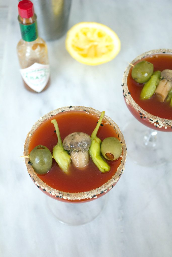 Overhead view of two dirty bloody mary martinis with bottle of tabasco and lemon half