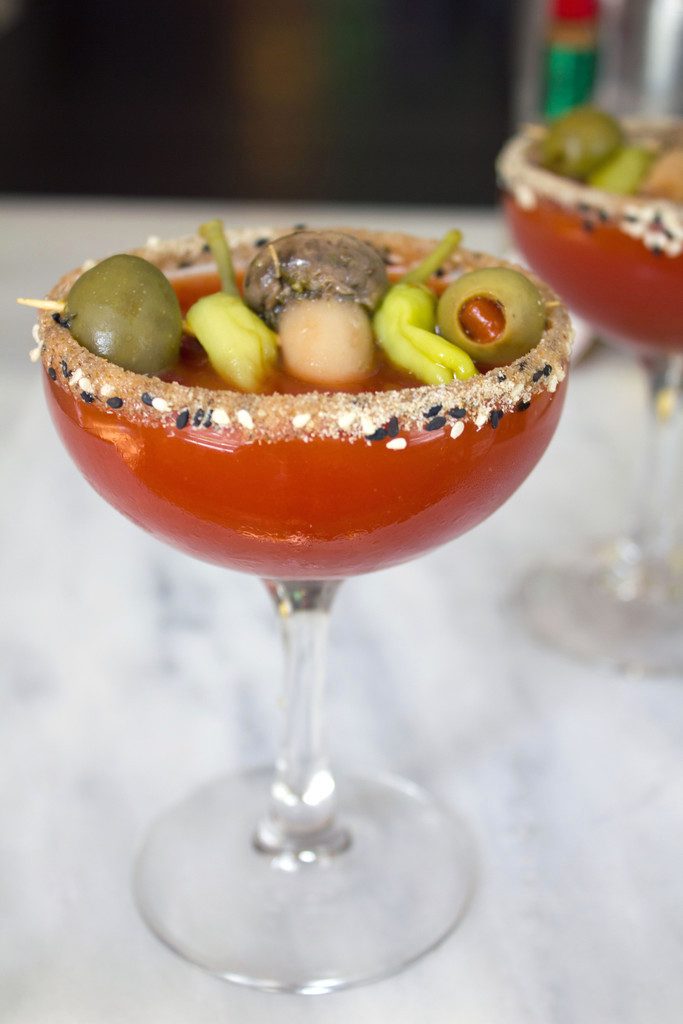 Head-on closeup view of a dirty bloody mary martini with salted rim and garnish