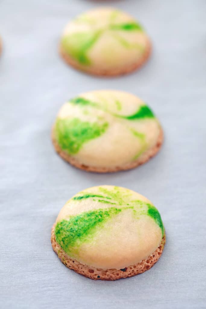 Head-on view of marbled green macarons just baked out of the oven