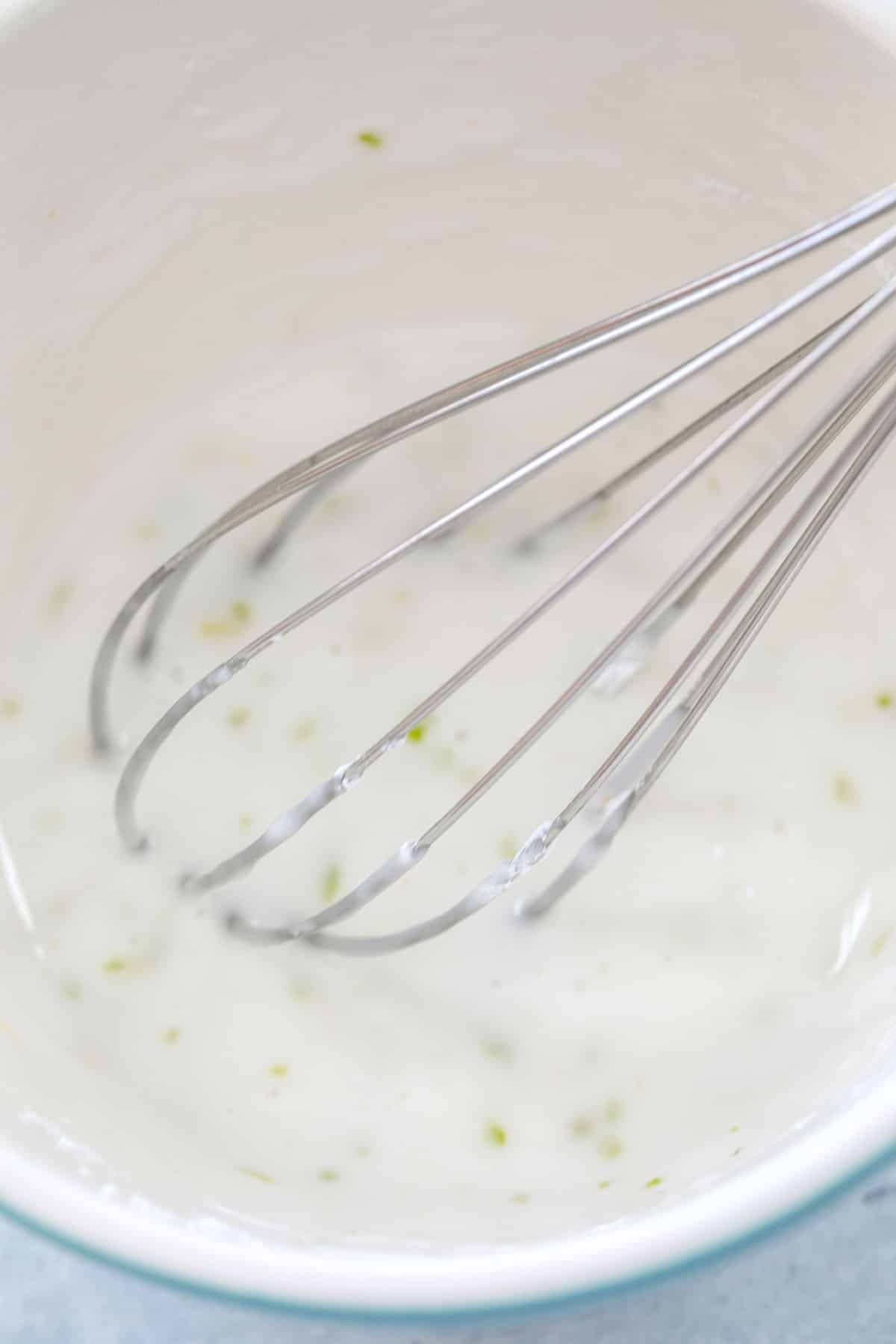 Overhead view of tequila icing being whisked in bowl with lime zest.