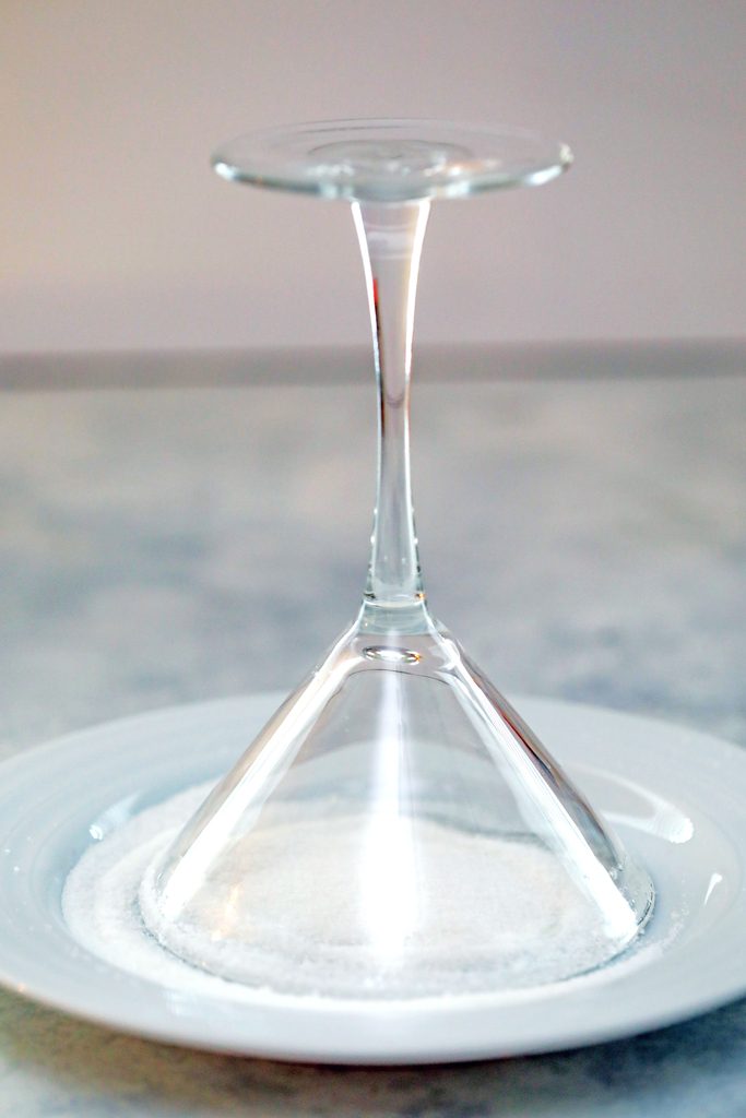 Head-on view of an upside-down martini glass on a plate of sugar to coat rim
