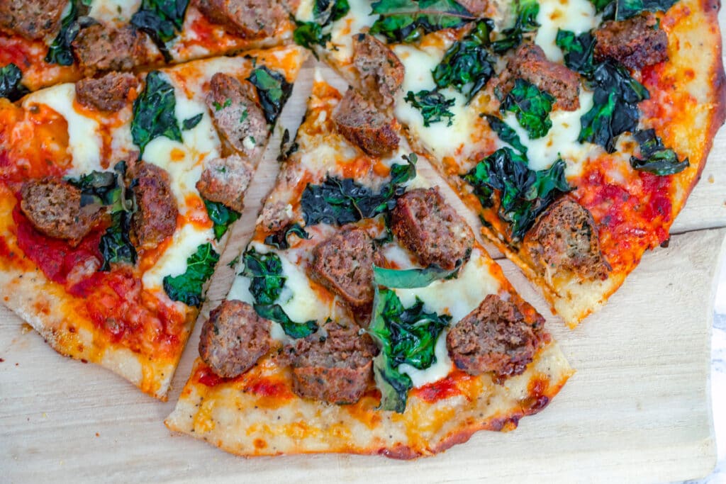 Landscape overhead view of meatball flatbread with kale, tomato sauce, and cheese, with one slice pulled out from rest of pizza