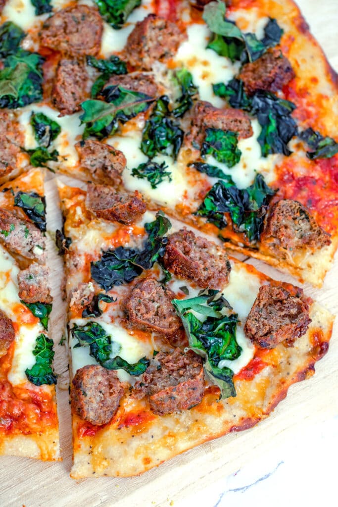 Overhead view of a slice of meatball flatbread with cheese and kale pulled out from the rest of the pizza