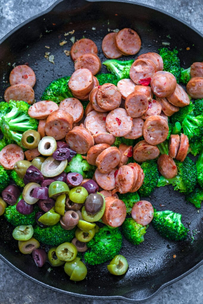 Overhead view of broccoli, kalamata olives, and chicken sausage in skillet