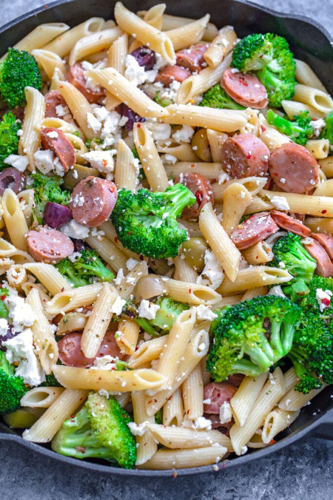 Overhead view of pasta, broccoli, chicken sausage, olives, and feta in skillet