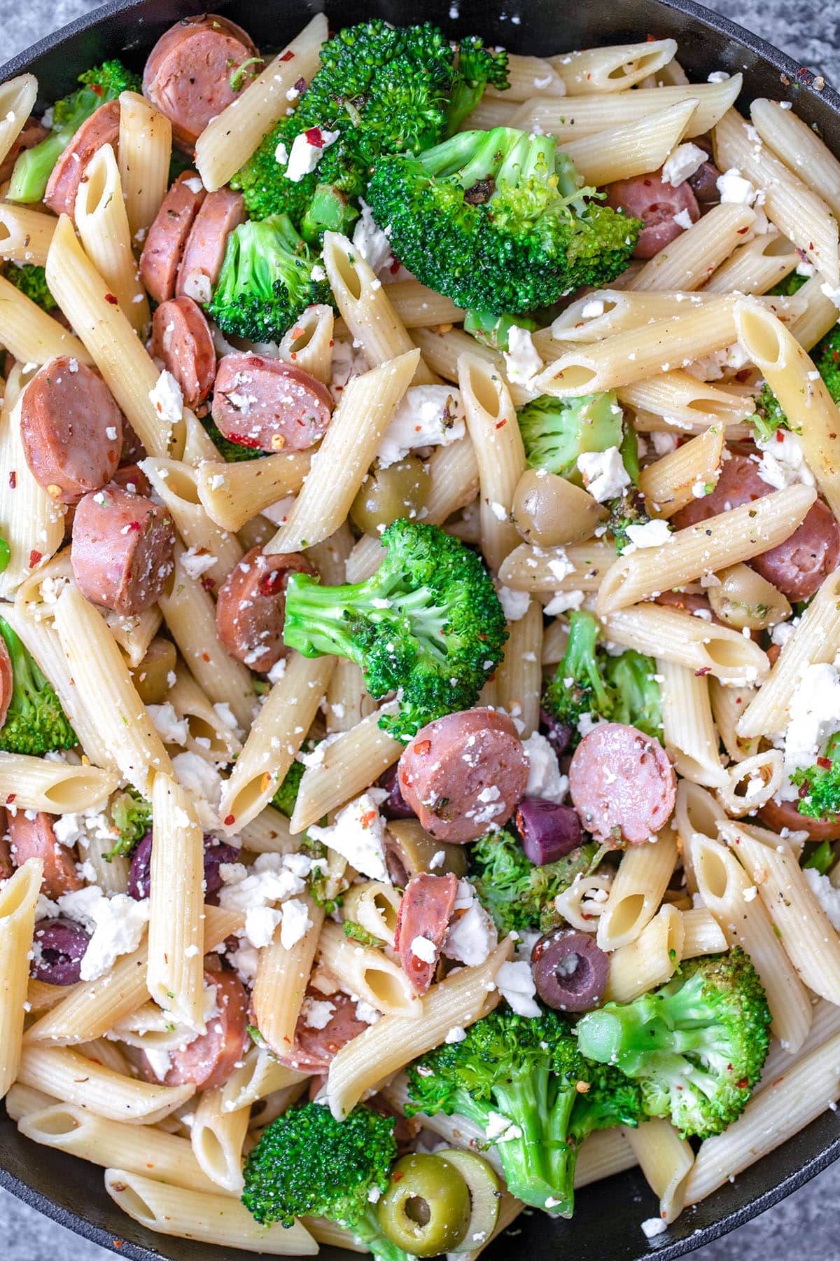 Overhead view of pasta, broccoli, chicken sausage, olives, and feta in skillet.