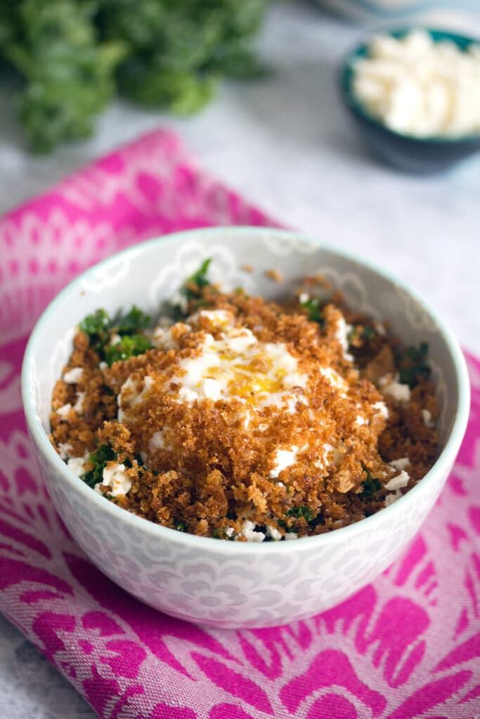 Head-on view of Mei Mei's Magical kale salad topped with a slow poached fried egg and crispy panko with feta cheese and a bunch of kale in background