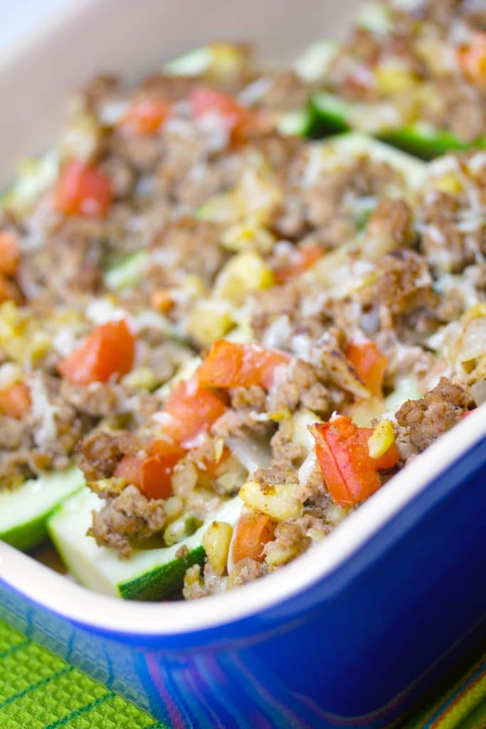 Sideways view of Mexican zucchini boats with turkey and tomatoes in a blue casserole dish