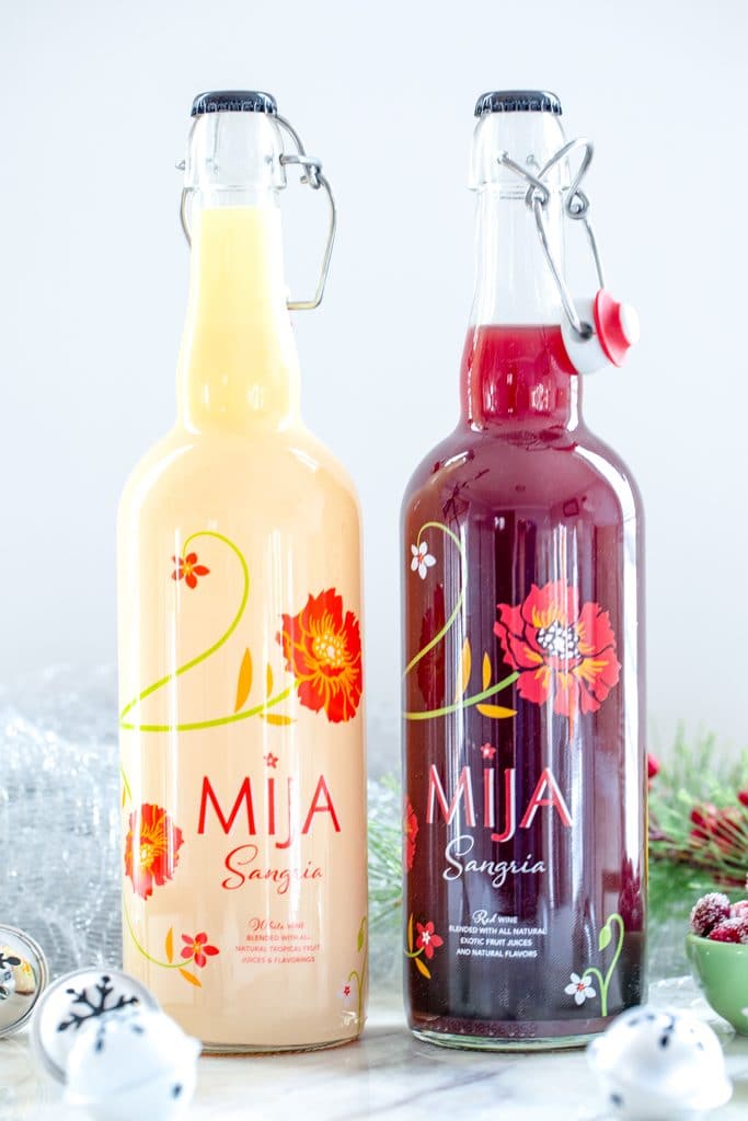 Head-on view of bottles of white and red Mija next to each other on a marble surface, surrounded by mini holiday bells