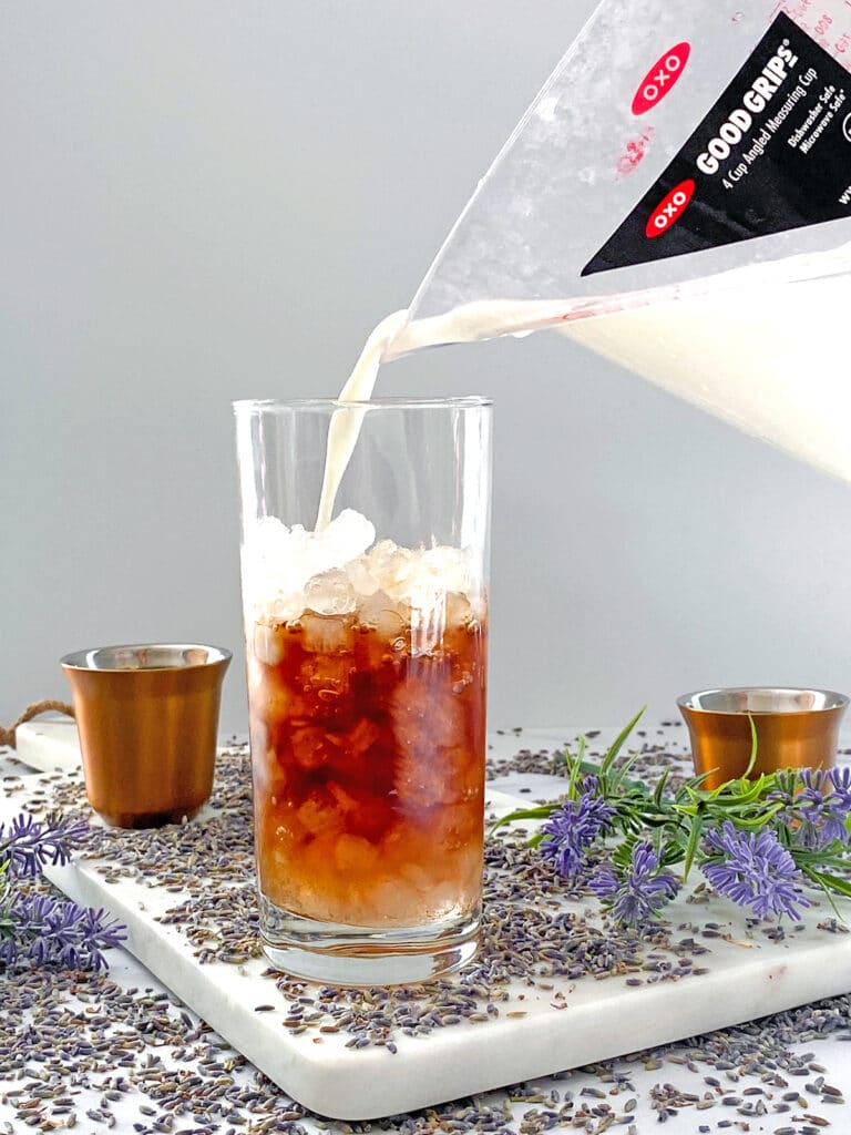 Milk being poured into ice-filled glass with coffee