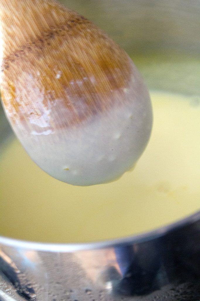 Closeup image of the back of a wooden spoon with custard mixture coating it to show it's thickened enough