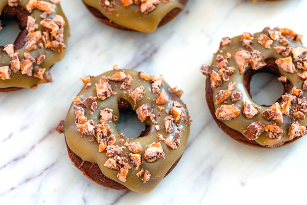 Landscape photo overhead view of multiple Milky Way doughnuts topped with caramel sauce and chopped Milky Ways on a marble surface