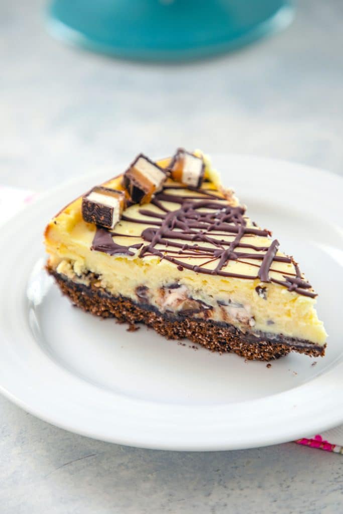 Head-on view of a slice of Milky Way cheesecake with chocolate drizzle on a white plate