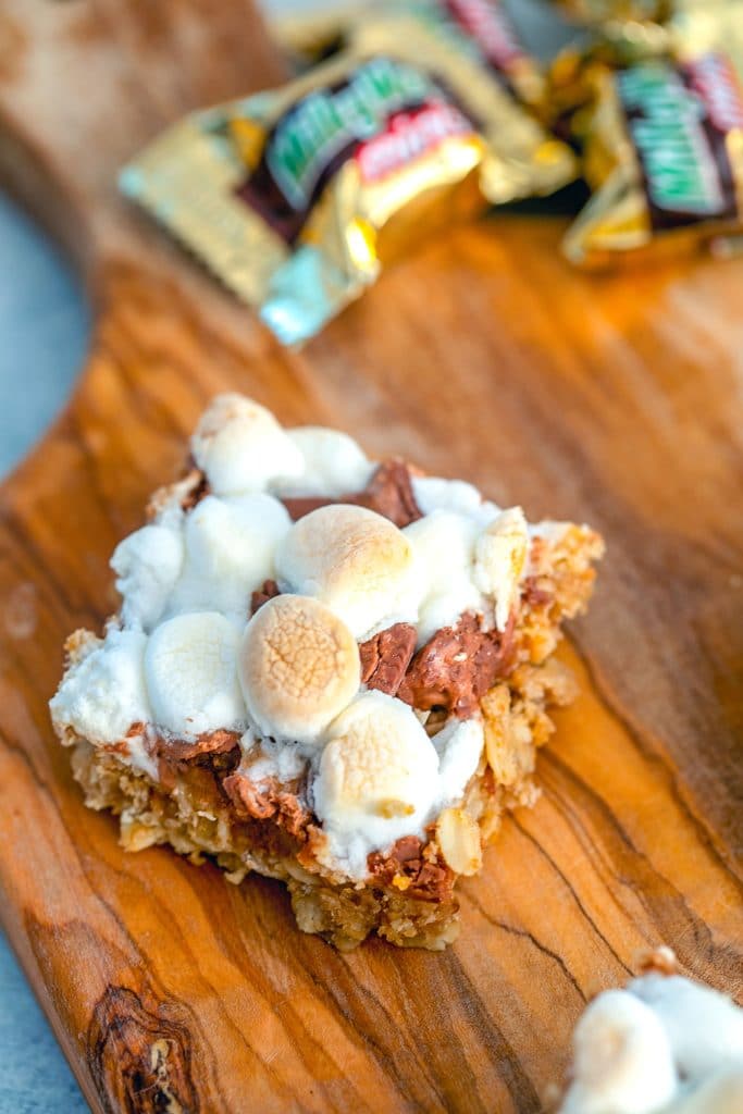 Overhead view of a Milky Way s'mores granola bar square on a wooden cutting board with mini Milky Ways in the background