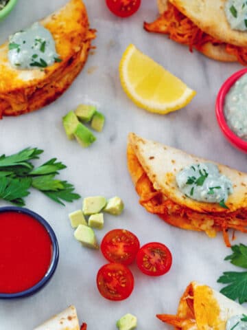 Overhead view of multiple buffalo chicken tacos topped with blue cheese sauce with tomatoes and avocado all around