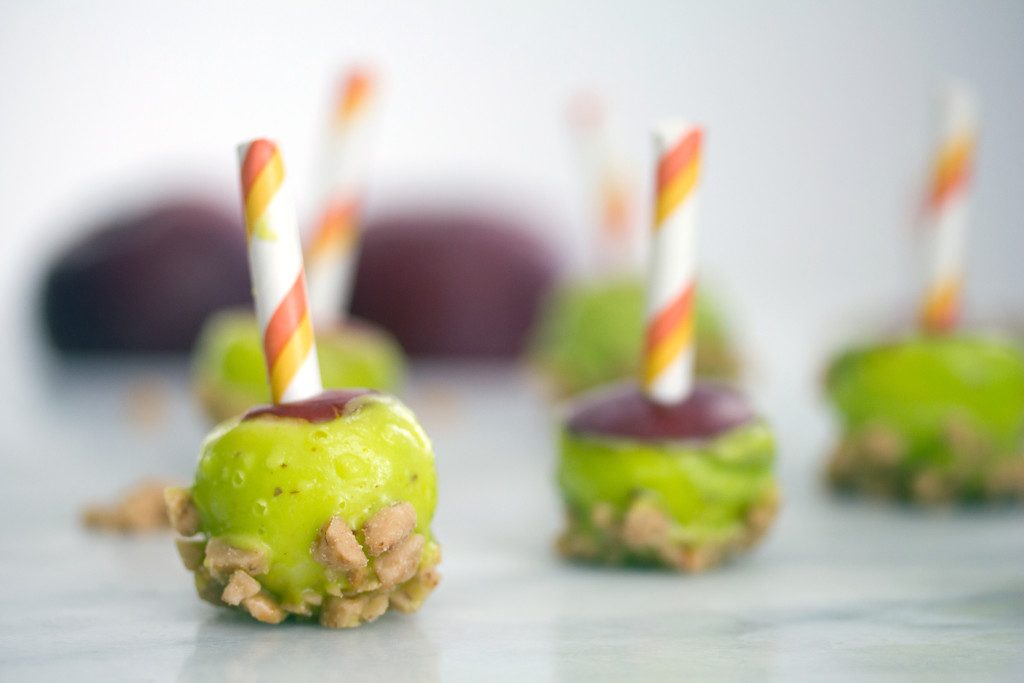 Landscape head-on view of multiple mini caramel candy apples with green candy melt coating and heath bar crunch all lined up