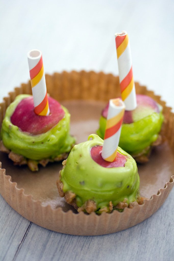 Overhead view of three mini caramel candy apples with green candy melts and heath bar pieces in a paper dessert cup