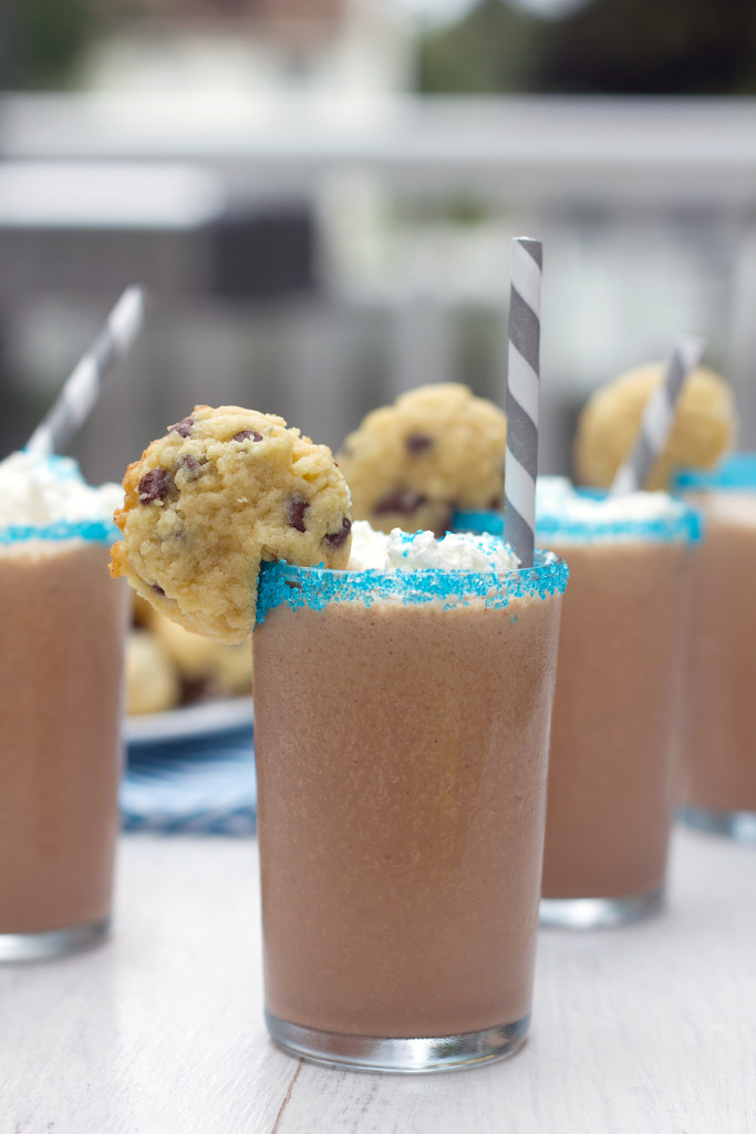 Head-on view of a row of mini milkshakes with blue sprinkles rims and mini chocolate chip cookie granishes
