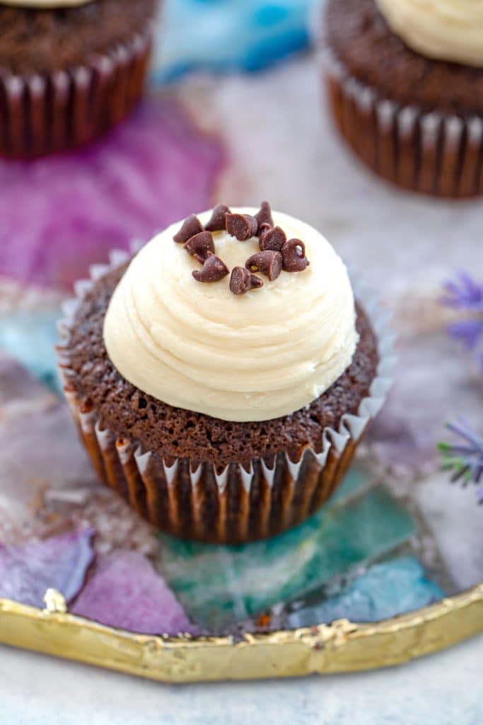 Overhead view of a chocolate mint chocolate chip cupcake topped with Baileys frosting and mini chocolate chips on a purple, green, and gold platter