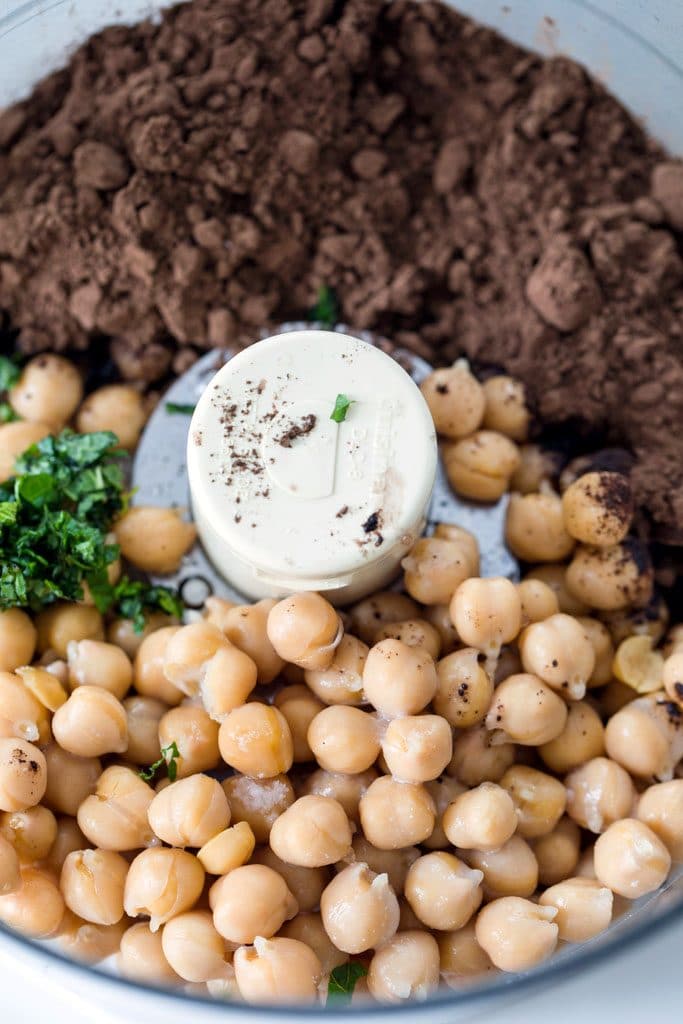 close-up bird's eye view of cocoa powder, chickpeas, mint, and coconut milk in food processor bowl