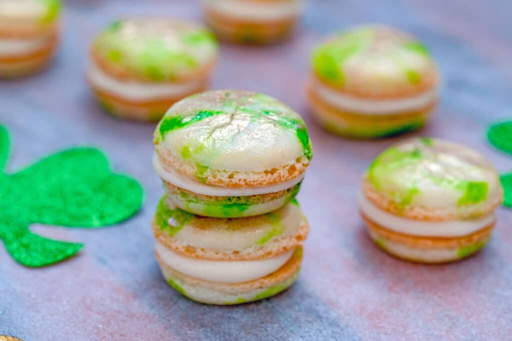 Head-on landscape view of a stack of mint macarons with Baileys buttercream with more macarons scattered around and glittery shamrocks
