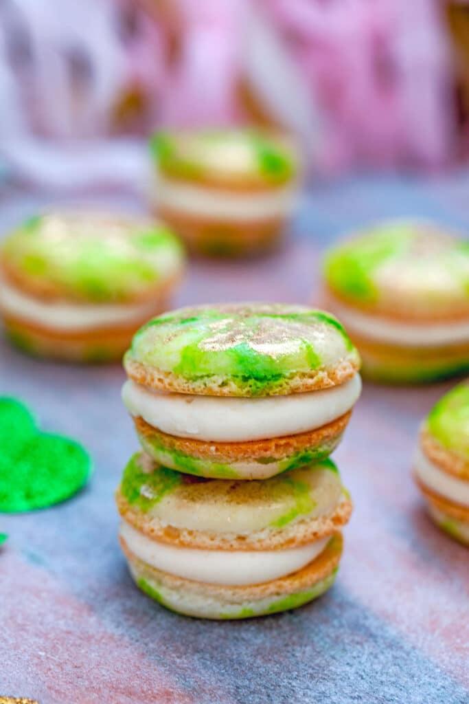 Head-on view of two mint macarons with Baileys buttercream stacked on top  of each other with more macarons and glittery shamrocks in the background