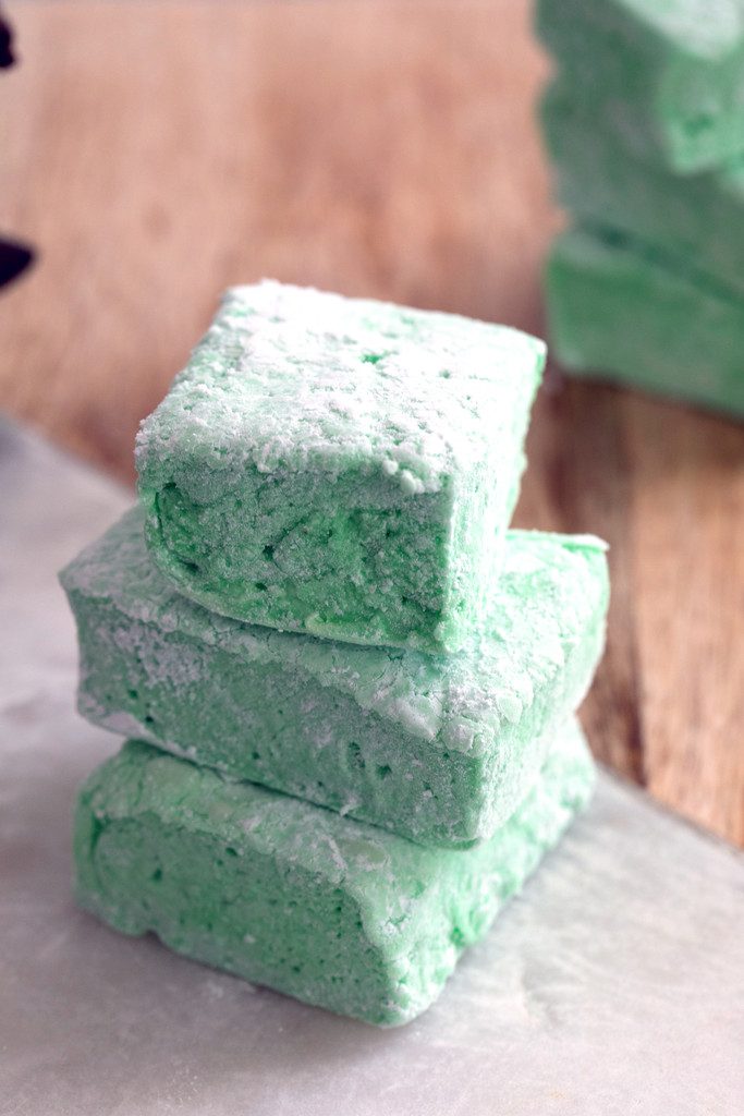 Head on view of three homemade green mint marshmallows stacked on top of each other on wood cutting board