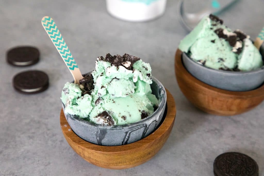 Landscape photo of two bowls of green mint oreo ice cream in metal and wood bowls with oreo cookies in the background