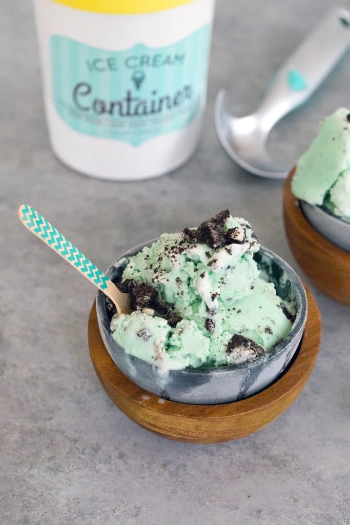 Bird's eye view of green mint oreo ice cream in metal and wood bowl with pint of ice cream and ice cream scoop in the background