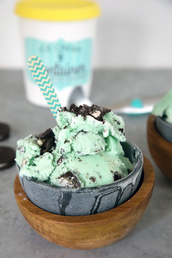 Close-up photo of green mint oreo ice cream in metal and wood bowls with pint of ice cream in the background