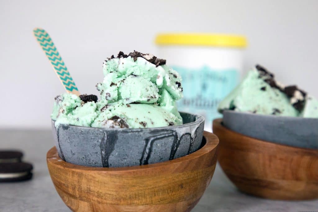 Head-on landscape photo of two metal and woods bowls filled with light green mint oreo ice cream with pint of ice cream in the background