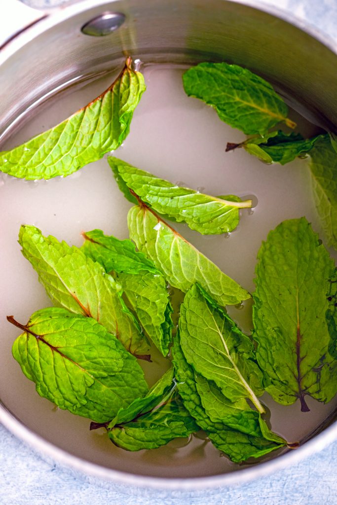 Overhead view of sugar, water, and fresh mint leaves in a saucepan about to come to a boil for mint simple syrup