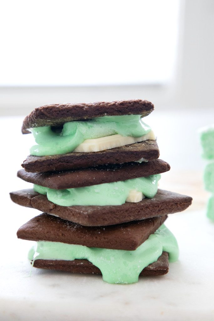 Head-on view of stack of three mint white chocolate s'mores made with chocolate graham crackers and oozing green mint marshmallows
