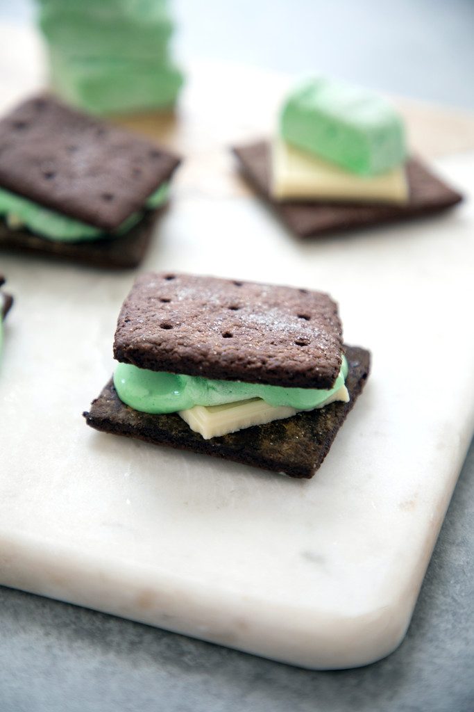 Overhead view of mint white chocolate s'mores with chocolate graham crackers and green mint marshmallows sitting on marble board