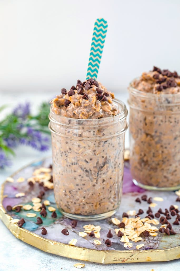 Head-on view of two jars of mocha overnight oats on a colorful plate with oats and mini chocolate chips and flowers in the background