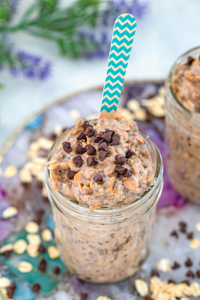 Overhead view of a jar of mocha overnight oats with mini chocolate chips on top and a colorful spoon on a colorful plate with oats and mini chocolate chips scattered around