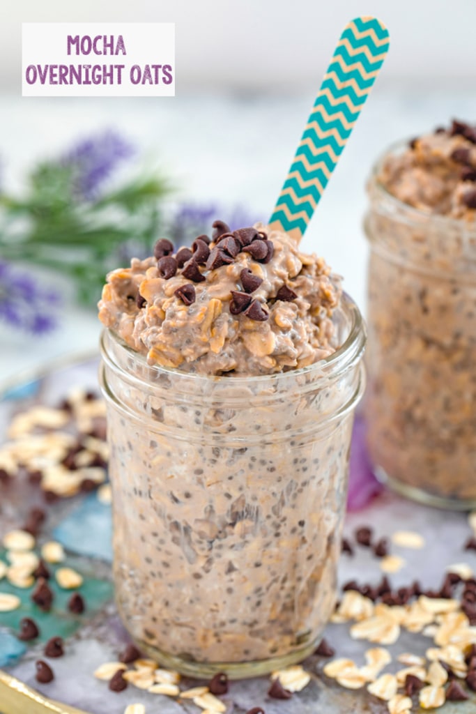 Head-on view of a jar of mocha overnight oats on a colorful plate with oats and mini chocolate chips scattered around, second jar and flowers in the background, and recipe title at top