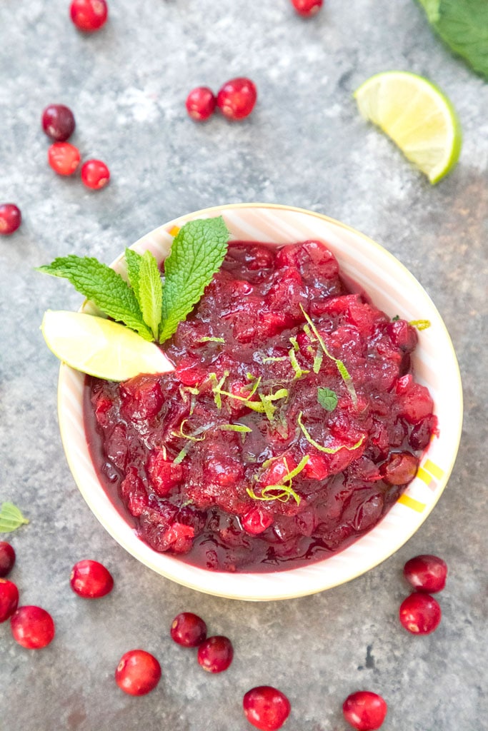 Overhead view of a bowl of mojito cranberry sauce with lime wedge and mint garnish surrounded by fresh cranberries