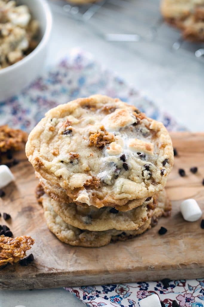 Overhead view of a stack of Momofuku Milk Bar Cornflake Marshmallow Cookies on a wooden board with mini marshmallows, chocolate chips, and cornflake crunch scattered around