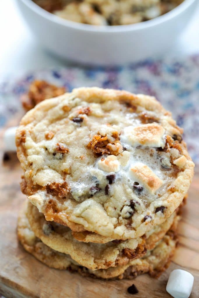 A closeup of the top cookie on a stack of Momofuku Milk Bar Cornflake Chip Marshmallow Cookies on a wooden board with a bowl of cookie dough in the background