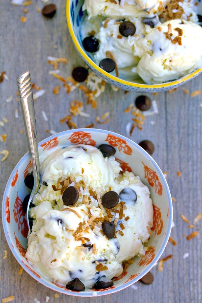 Overhead view of two bowls of Mounds bar ice cream with toasted coconut and dark chocolate chips scattered around