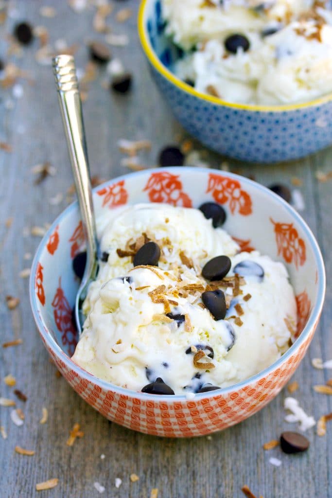 Red bowl of Mounds Bar Ice Cream with dark chocolate chips and toasted coconut with second bowl in the background and recipe title at top
