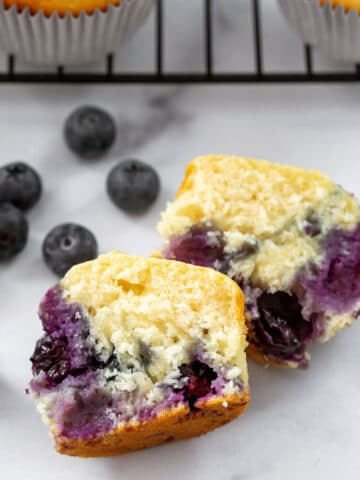 Closeup overhead view of a blueberry muffin cut in half with blueberries all around