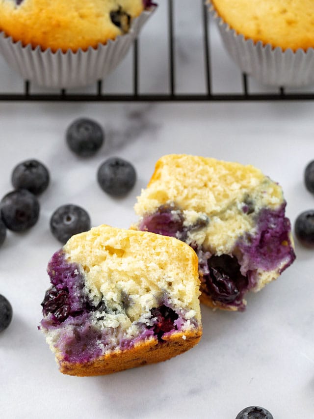 Overhead view of a blueberry muffin with pancake mix cut in half with muffins on rack and blueberries in background
