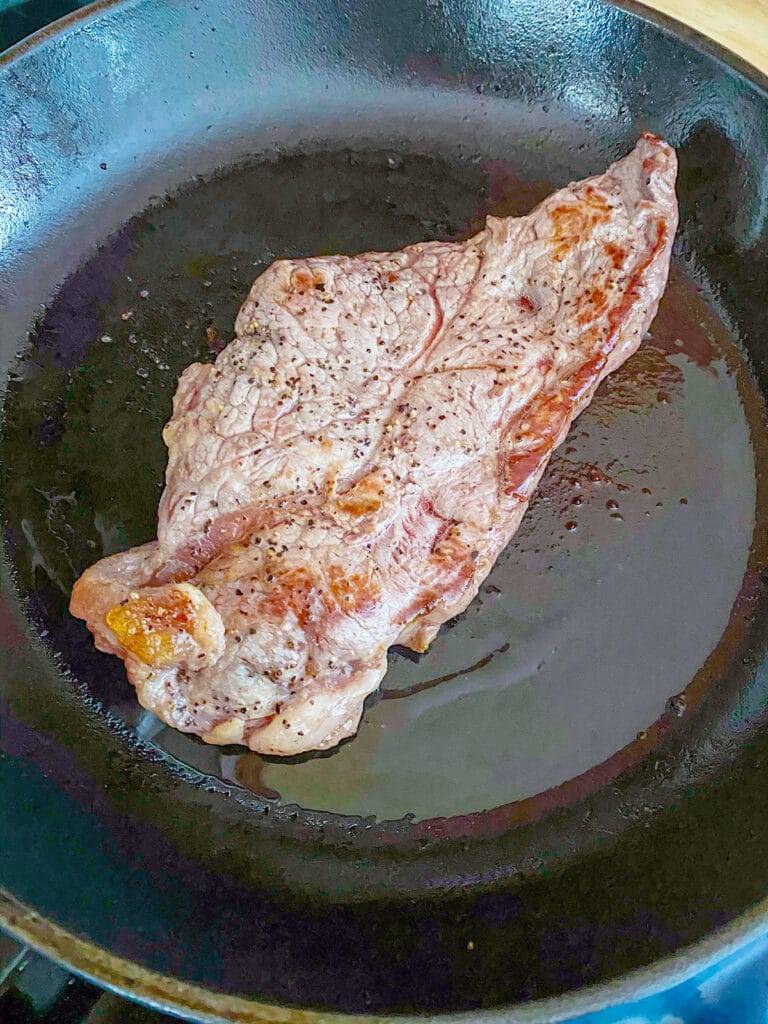 NY strip steak cooking in cast iron skillet.
