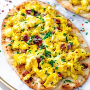 Closeup view of a naan breakfast pizza with scrambled eggs, crumbled bacon, and parsley.