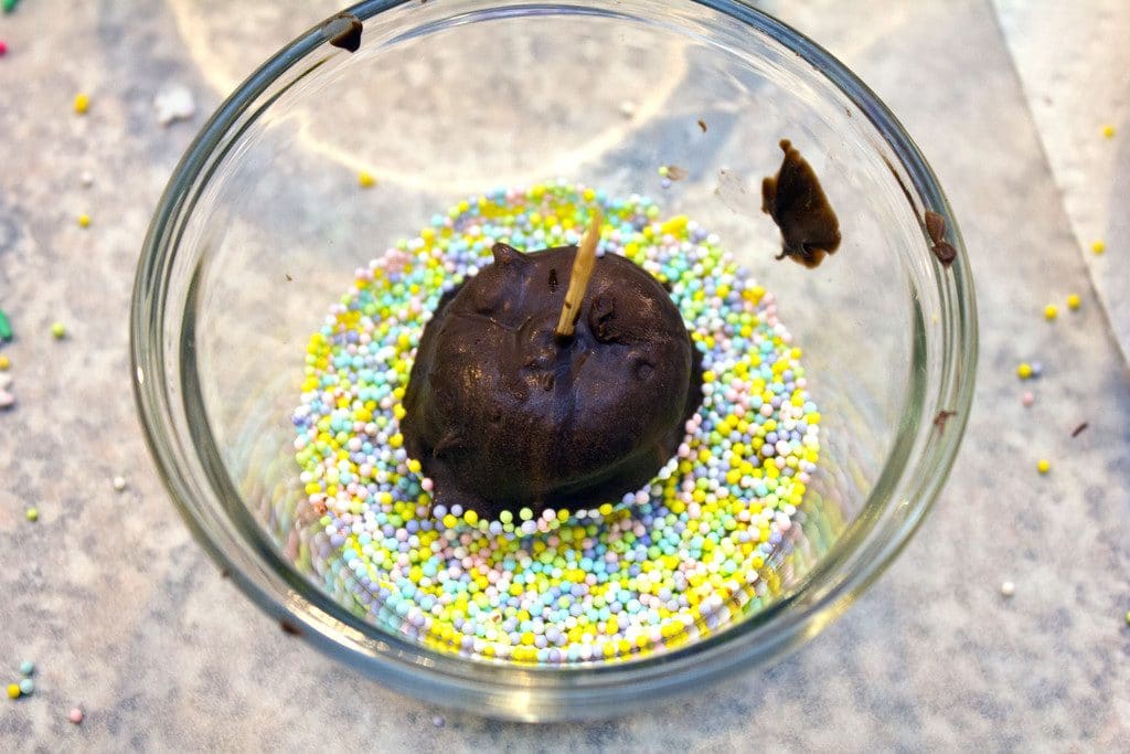 Nutella chocolate covered banana on a toothpick being dipped into sprinkles