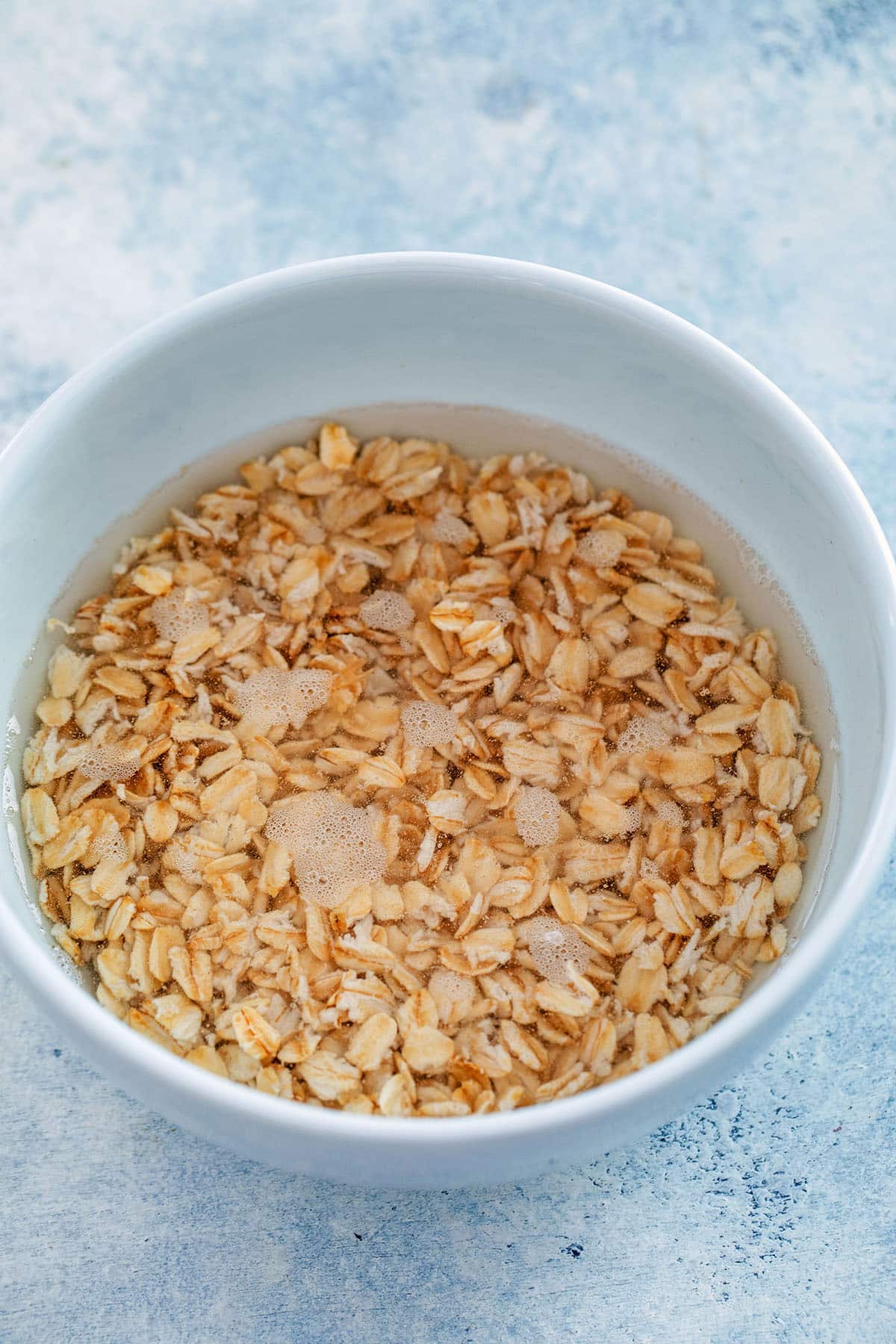 Overhead view of a white bowl of old-fashioned oats and water before going into the microwave.